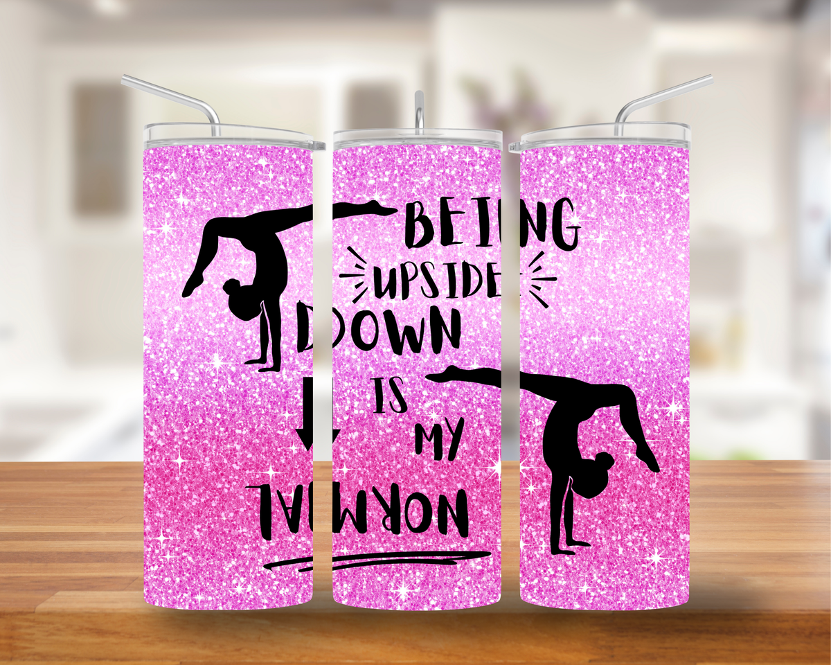 A pink and white ombre glitter tumbler with the text 'BEING UPSIDE DOWN IS MY NORMAL' and illustrations of gymnastic flips.